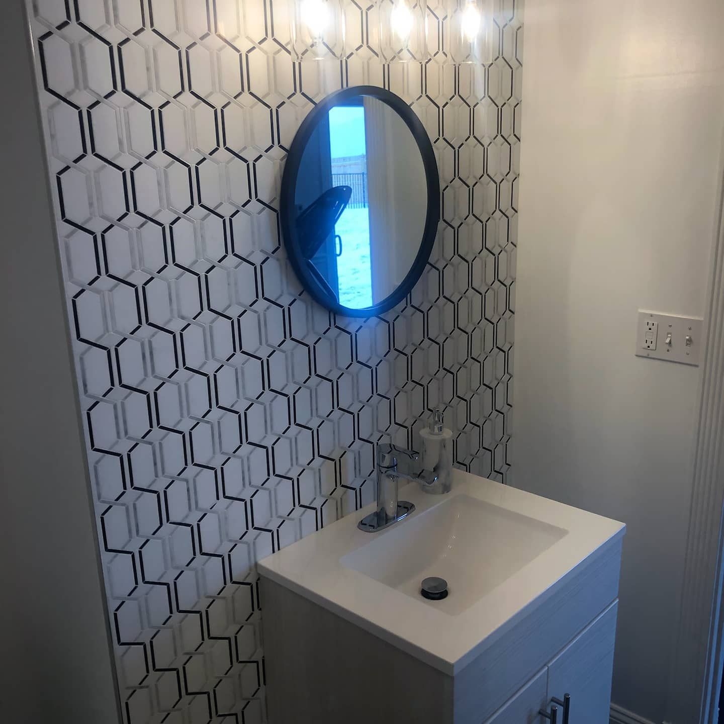 Small bathroom with white sink, oval mirror, and honeycomb-patterned wallpaper.