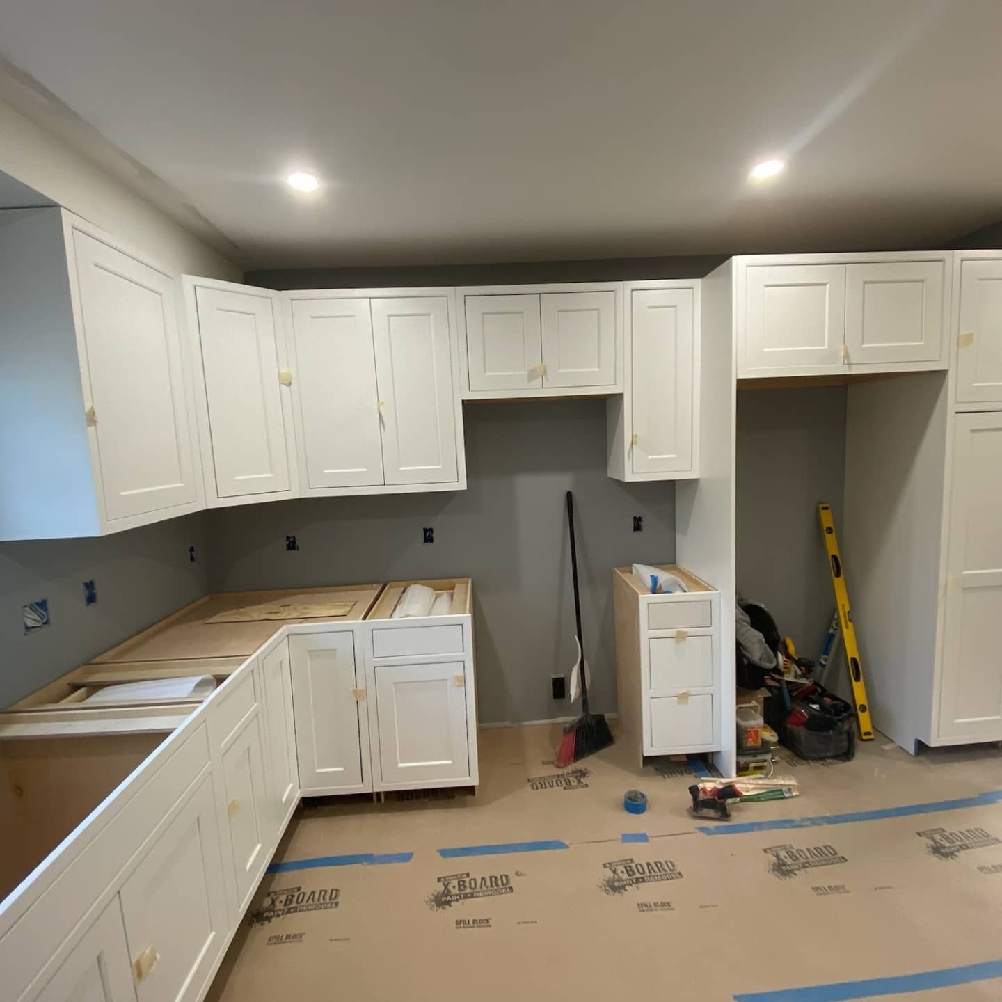 Kitchen under construction with white cabinets against a gray wall.