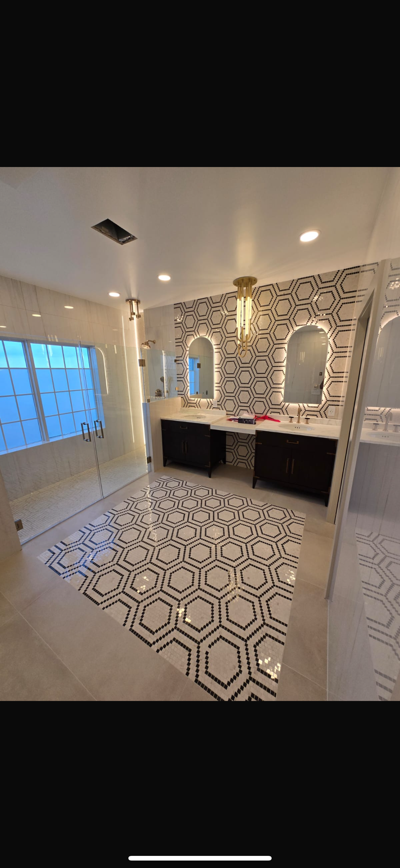 Bathroom with hexagon tile floor, black vanity, and arch mirrors.  Shower with window. Gold light fixture.