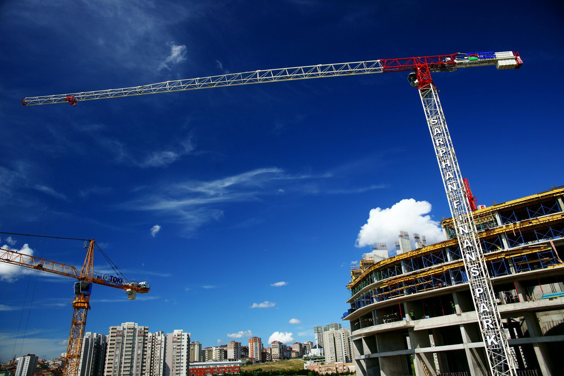Construction cranes at a building site against a bright blue sky.