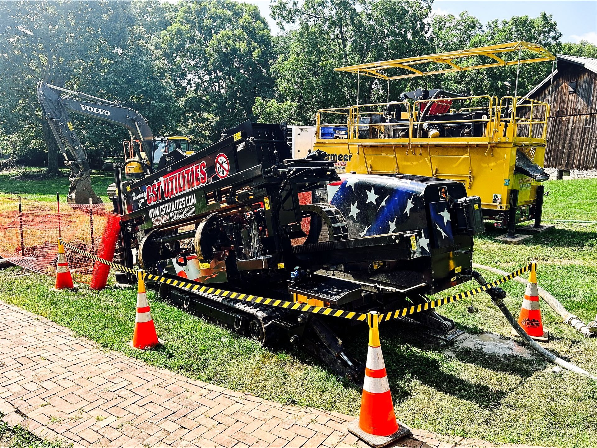 Black machinery and a yellow scaffolded vehicle on grass, surrounded by orange cones and caution tape.