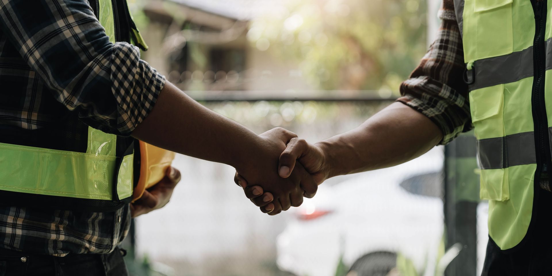 Two construction workers are shaking hands on a construction site.