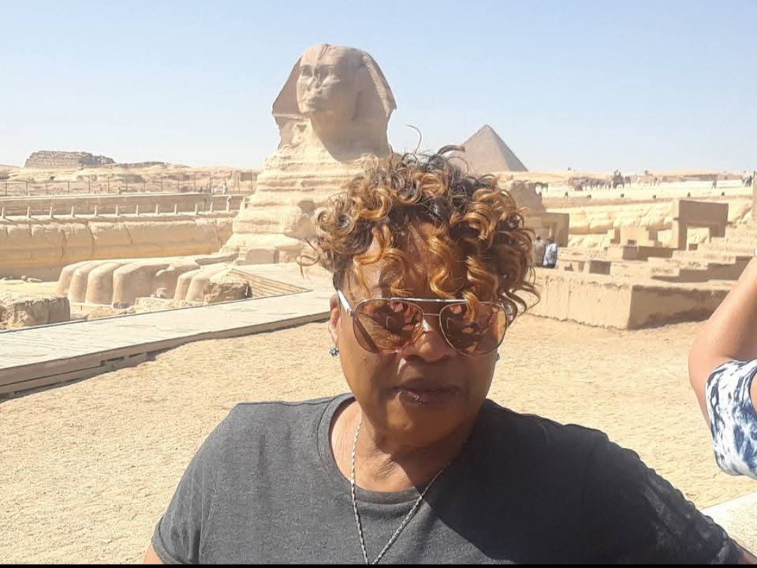 A woman wearing sunglasses is standing in front of a pyramid.