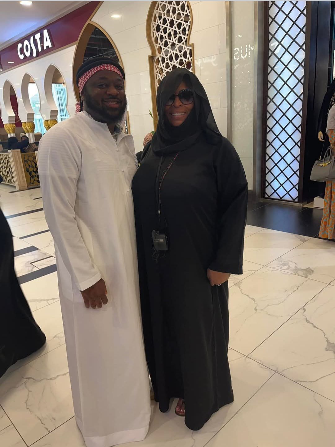A man and a woman are posing for a picture in front of a costa store.