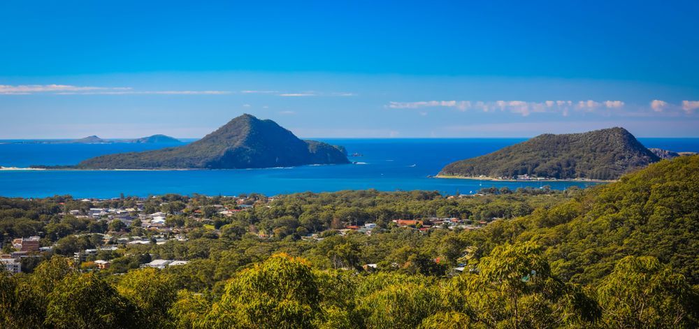 There Are Two Mountains In The Distance And A Body Of Water In The Foreground — East Coast Air In Port Stephens, NSW