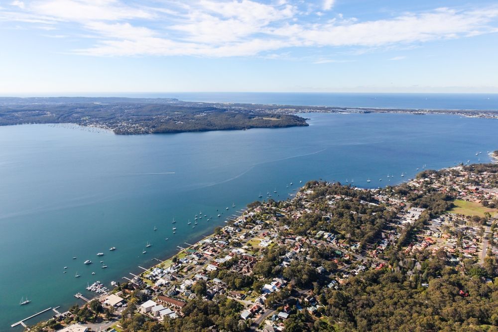 An Aerial View Of A Large Body Of Water Surrounded By Houses And Trees — East Coast Air In Lake Macquarie, NSW