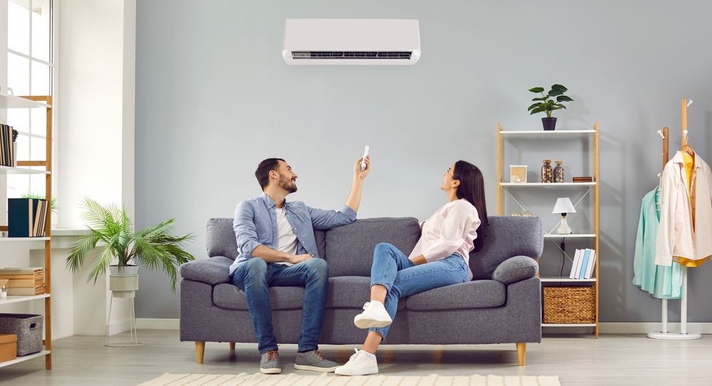 A Man And A Woman Are Sitting On A Couch In Front Of An Air Conditioner — East Coast Air In Singleton, NSW