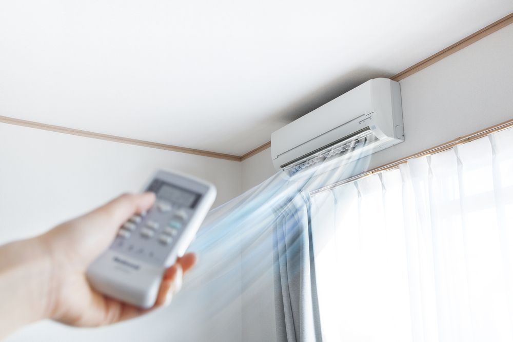 Hand Holding Remote, Aiming at A Wall-Mounted Air Conditioner — East Coast Air In Raymond Terrace, NSW