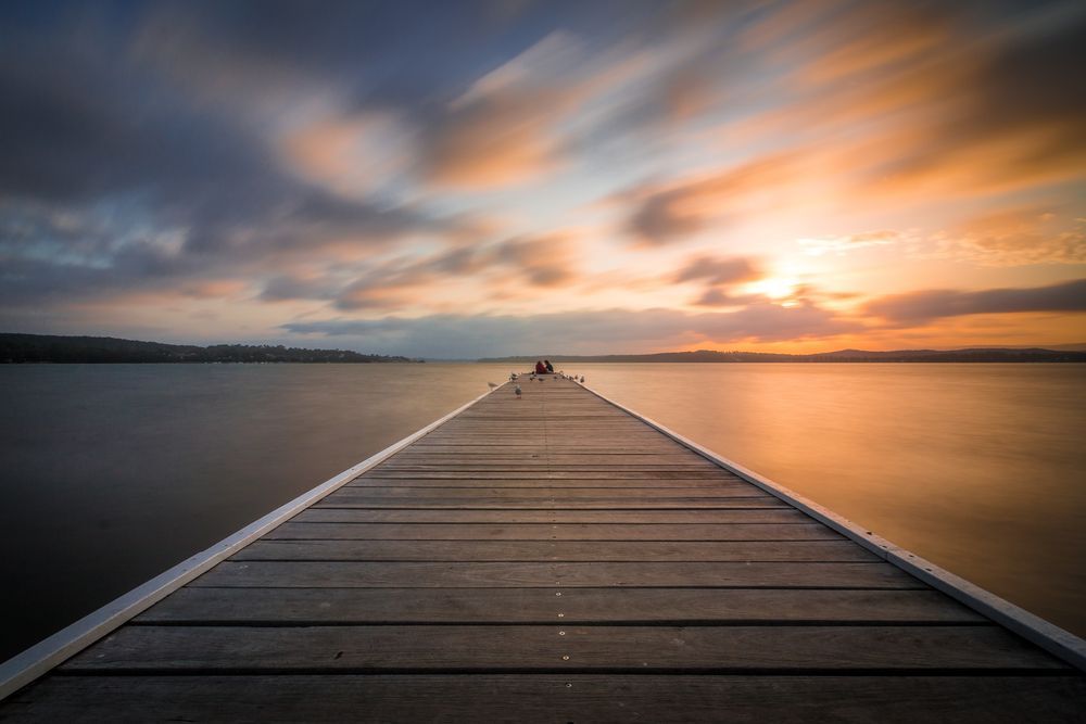 A Long Wooden Dock Leading Into A Body Of Water At Sunset — East Coast Air In Lake Macquarie, NSW
