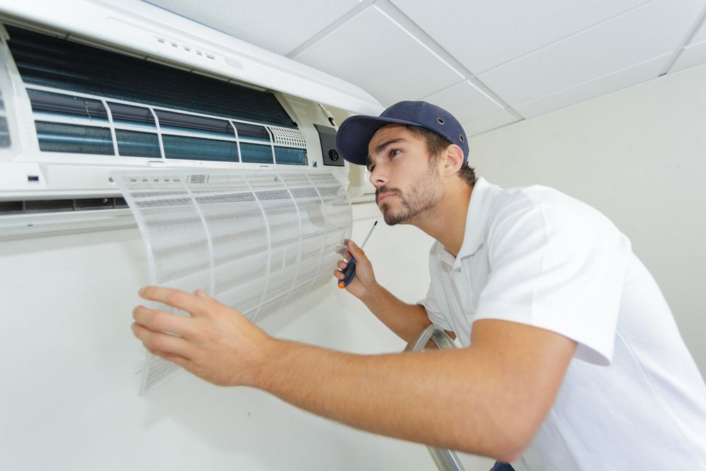 A Man Is Working On An Air Conditioner With A Screwdriver — East Coast Air In Cessnock, NSW
