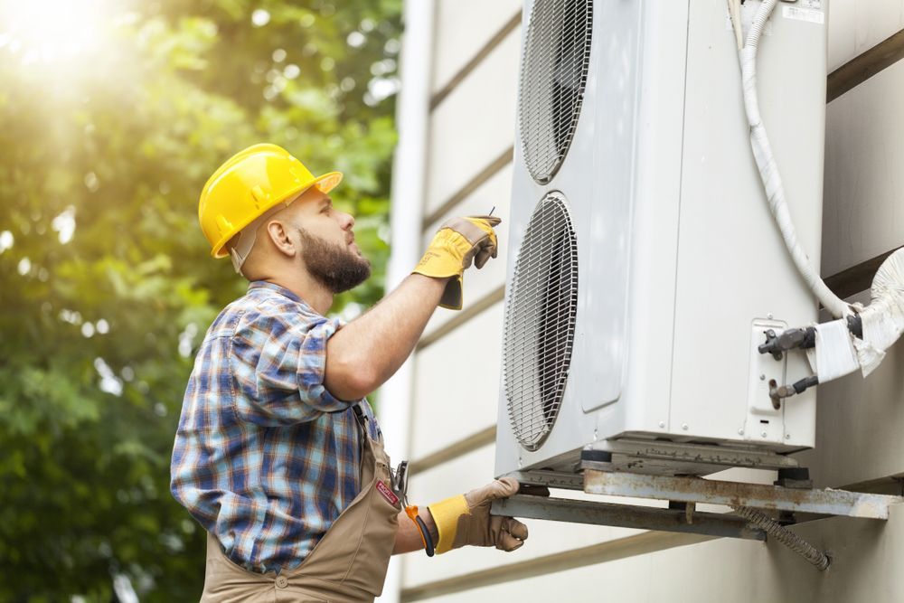 HVAC Technician in A Yellow Hard Hat, Inspecting an Outdoor Air Conditioning Unit on A Building — East Coast Air In Raymond Terrace, NSW