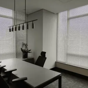 Um sofá secional cinza com almofadas coloridas em frente a três persianas que filtram a luz.