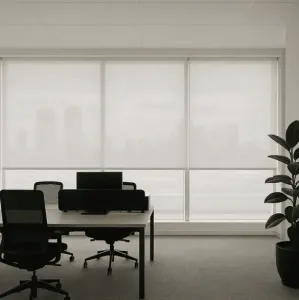 Interior de escritório com mesas, cadeiras, computadores e plantas em vasos perto de uma grande janela com persianas brancas.