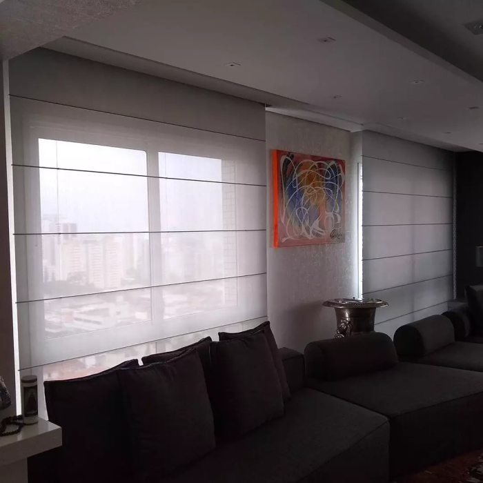 Sala de estar com cortinas romanas brancas, sofá cinza escuro e obras de arte coloridas.