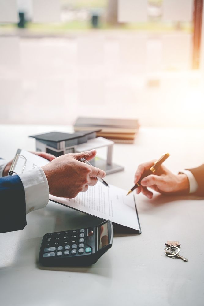 Hands signing a contract over a table, with a calculator, keys, and model house visible.