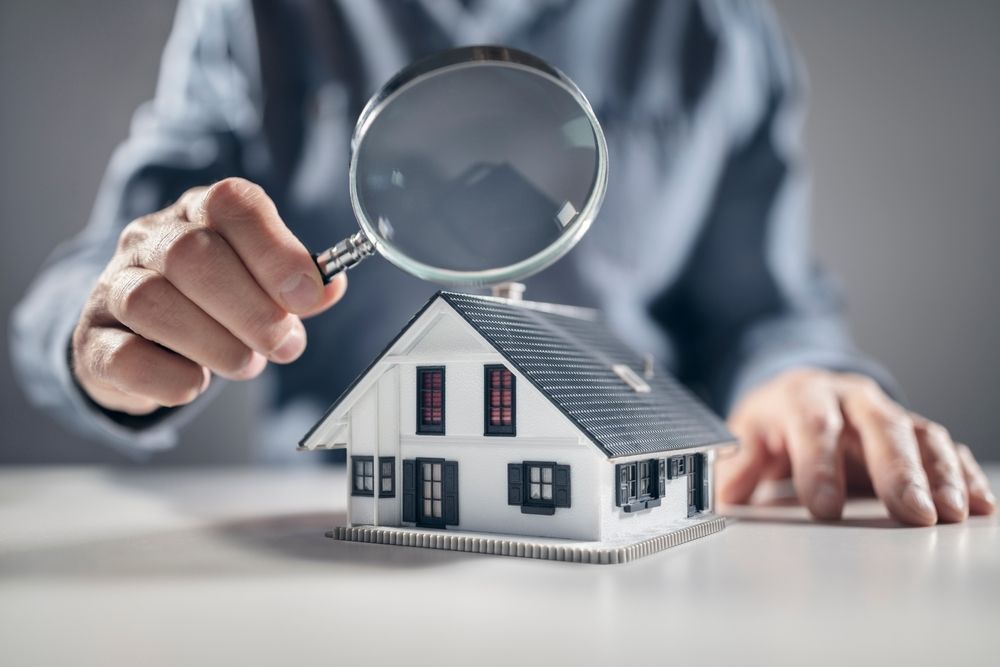 A person examining a miniature house with a magnifying glass.