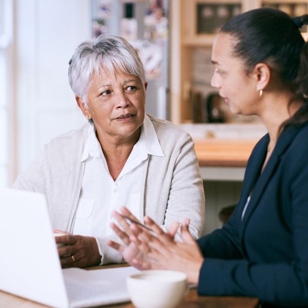 Two coworkers discussing at a table with a laptop and coffee cup in a bright office