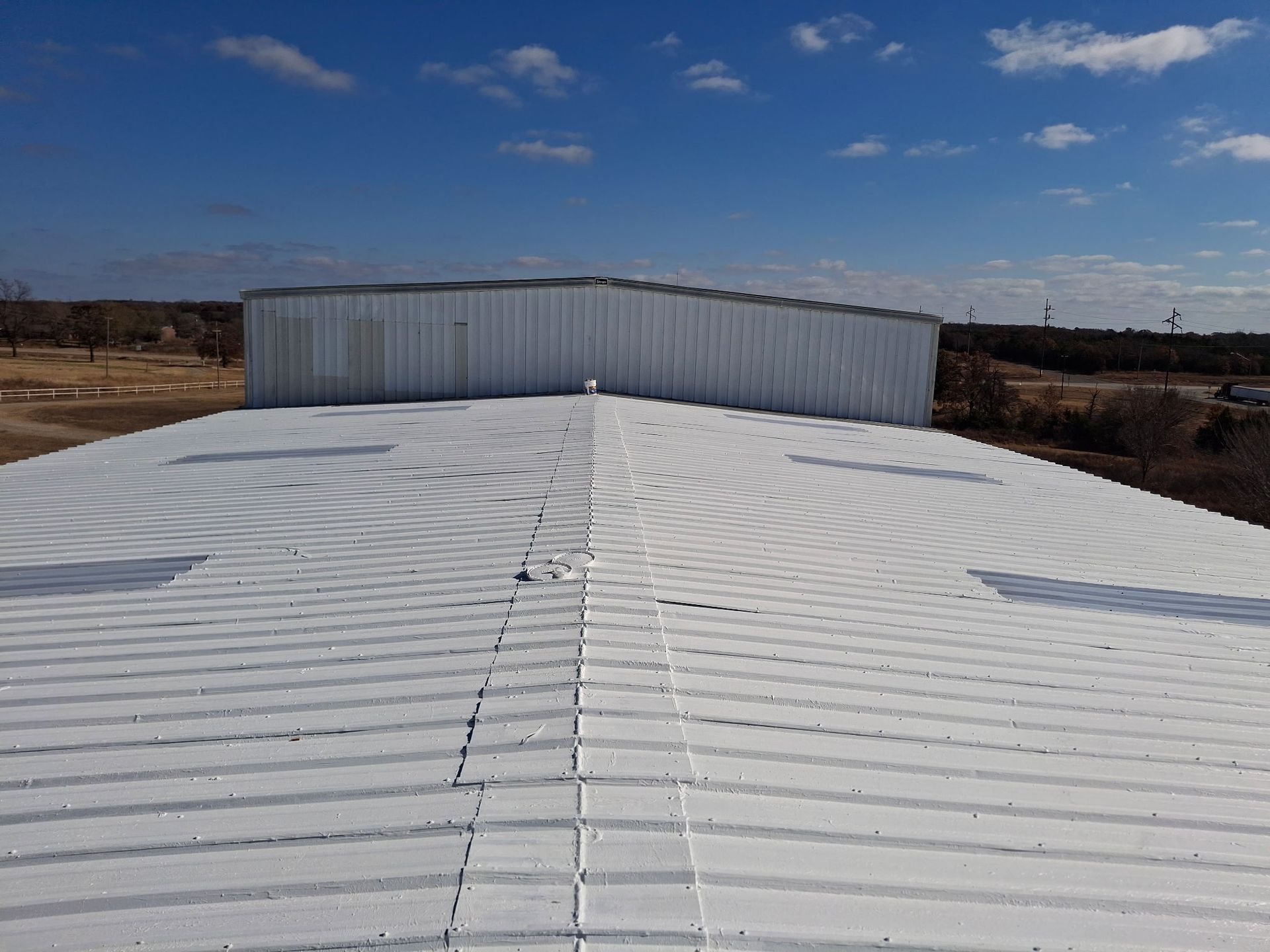 Worker on a ladder installing panels on a sloped roof at sunset