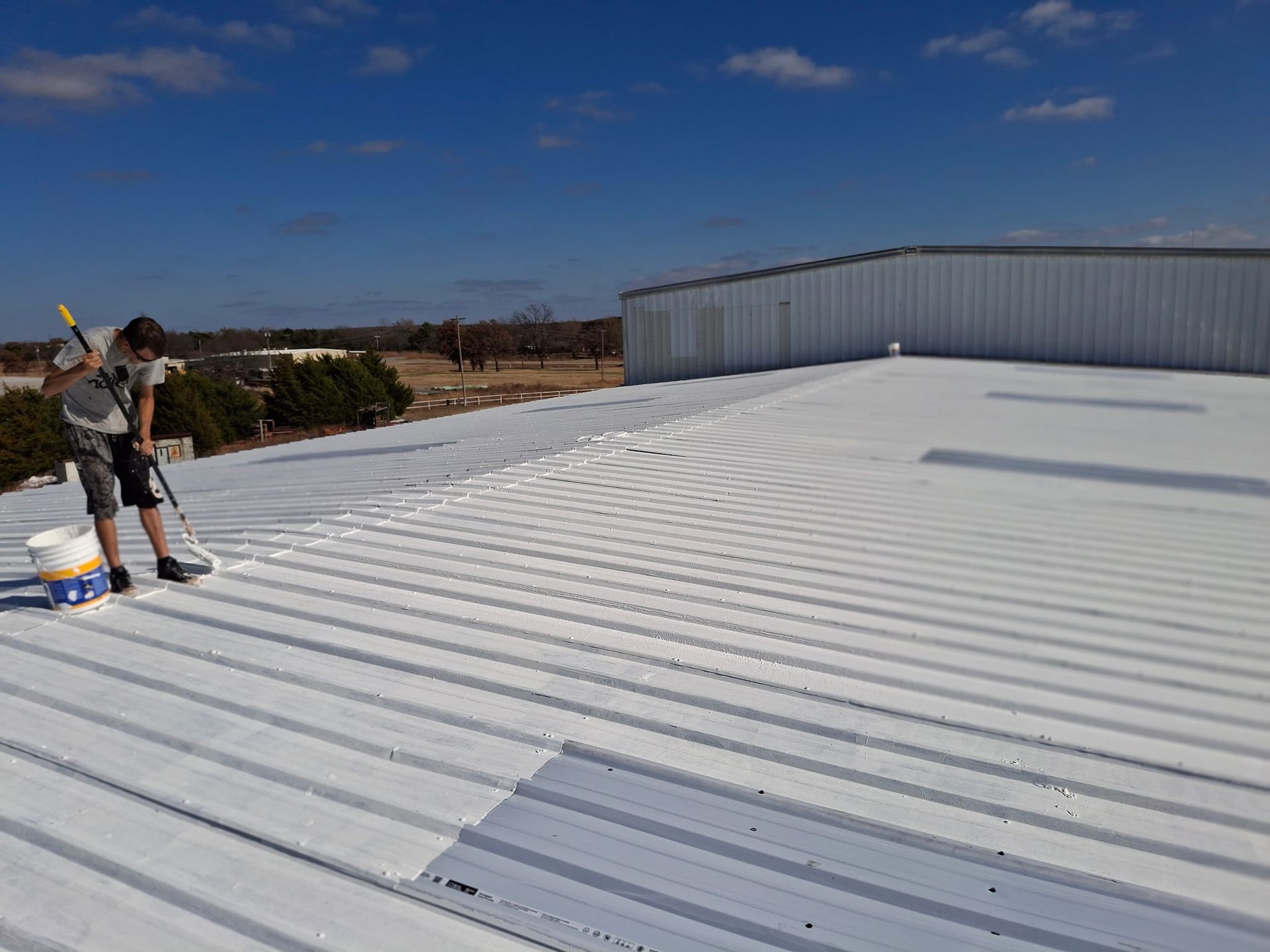 Worker in orange safety gear on a rooftop beside a white skylight.