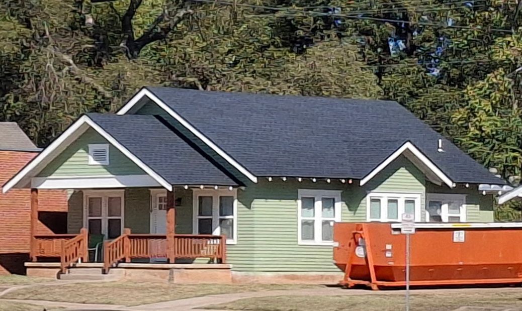 Person using a yellow-and-black roofing nailer on asphalt shingles, with an orange air hose attached