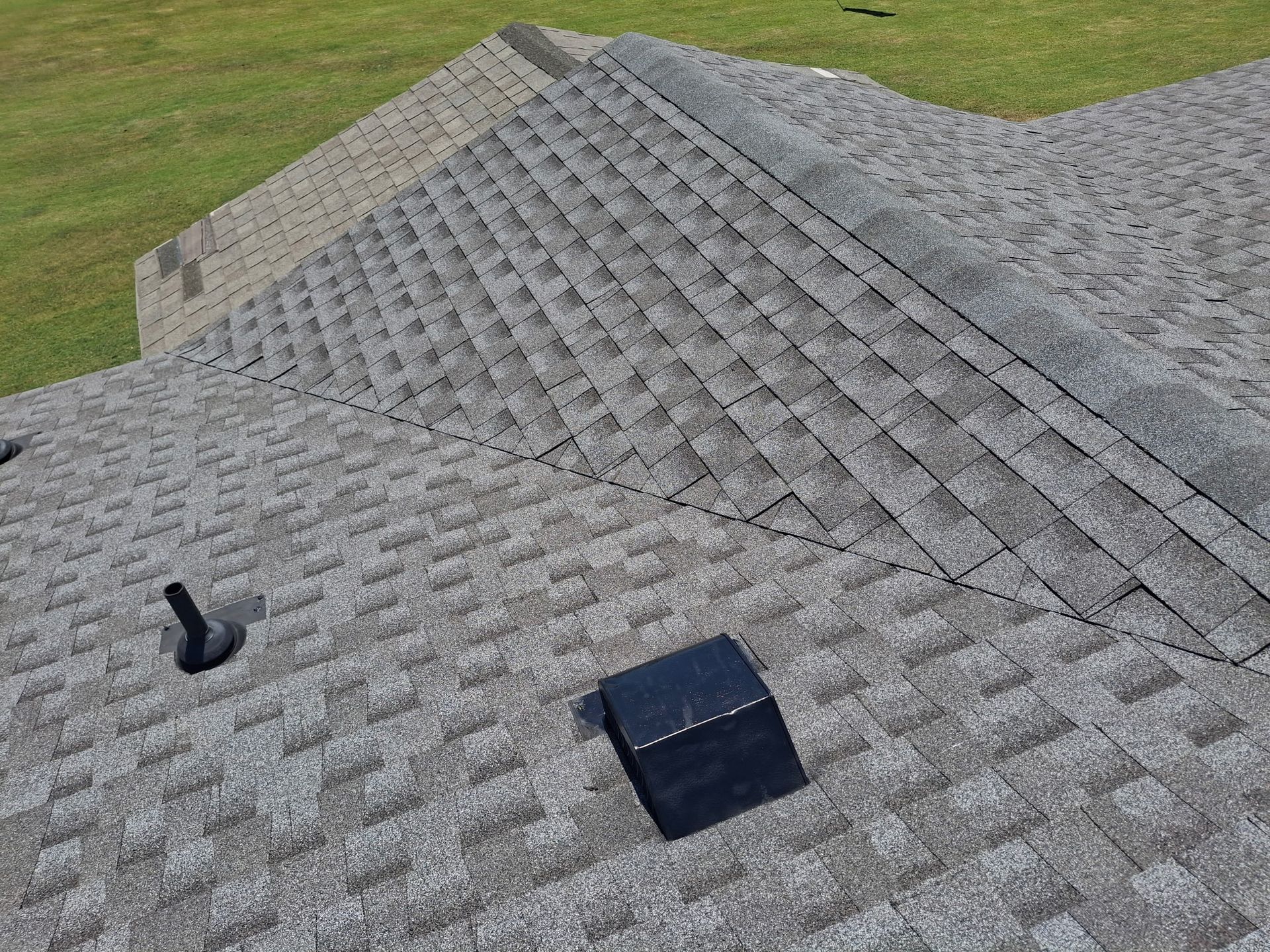 Aerial view of a suburban house with gray roof, driveway, and a tree-lined backyard patio.