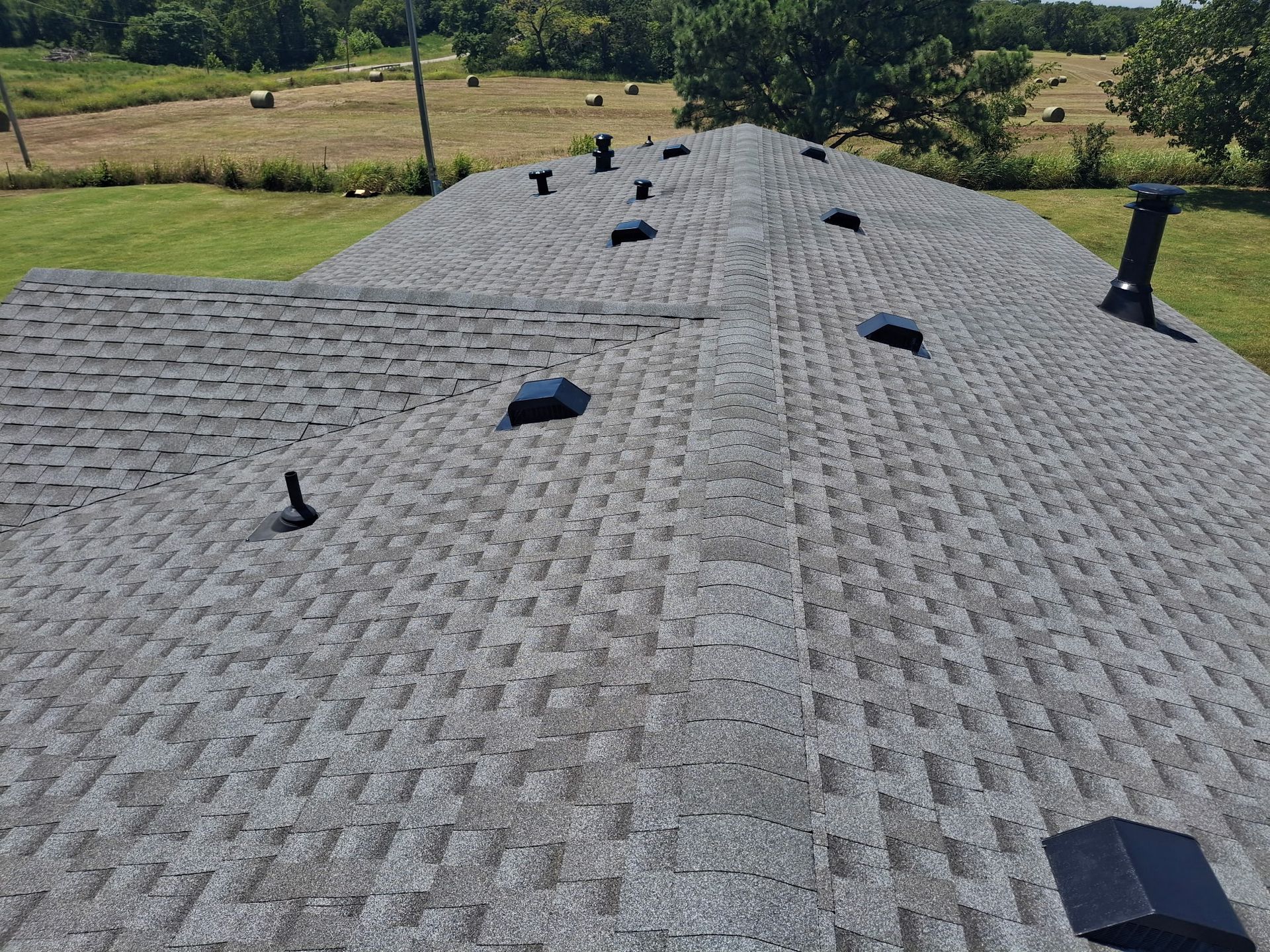 Worker in a yellow hard hat inspecting a shingled roof with a hammer.