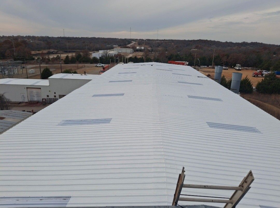 Rooftop under construction with gray shingles, vents, and trees under a blue sky