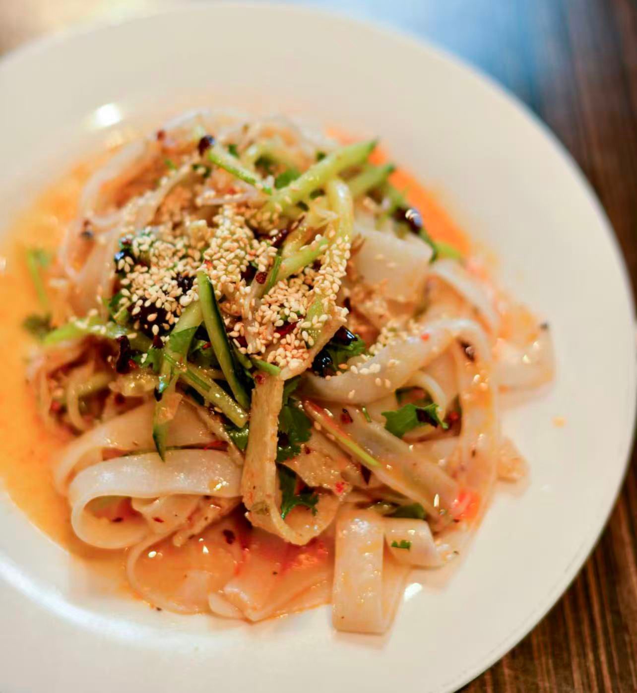 Plate of pasta topped with vegetables, sesame seeds, and sauce on a wooden table