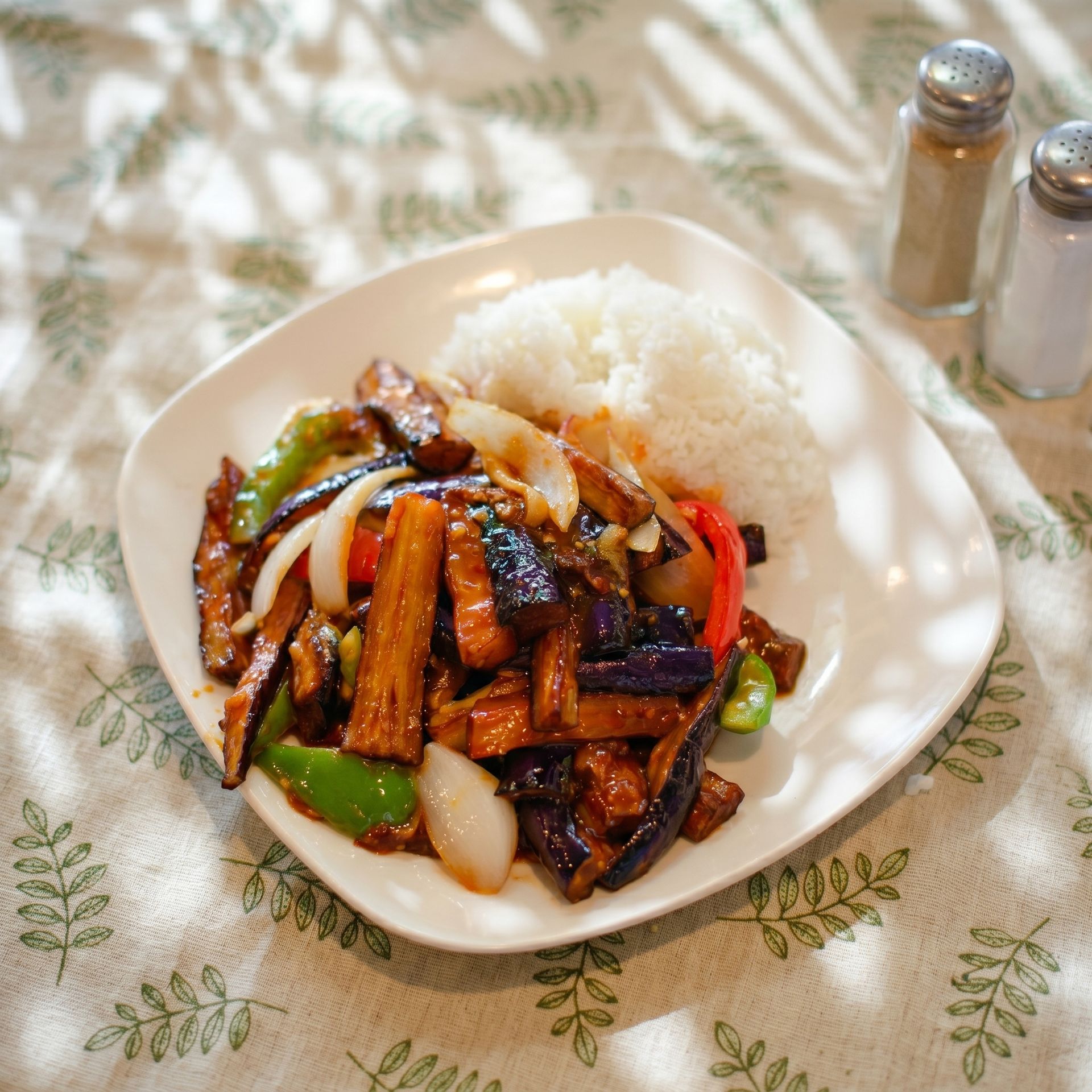 Plate of stir-fried vegetables and meat with white rice on a patterned tablecloth
