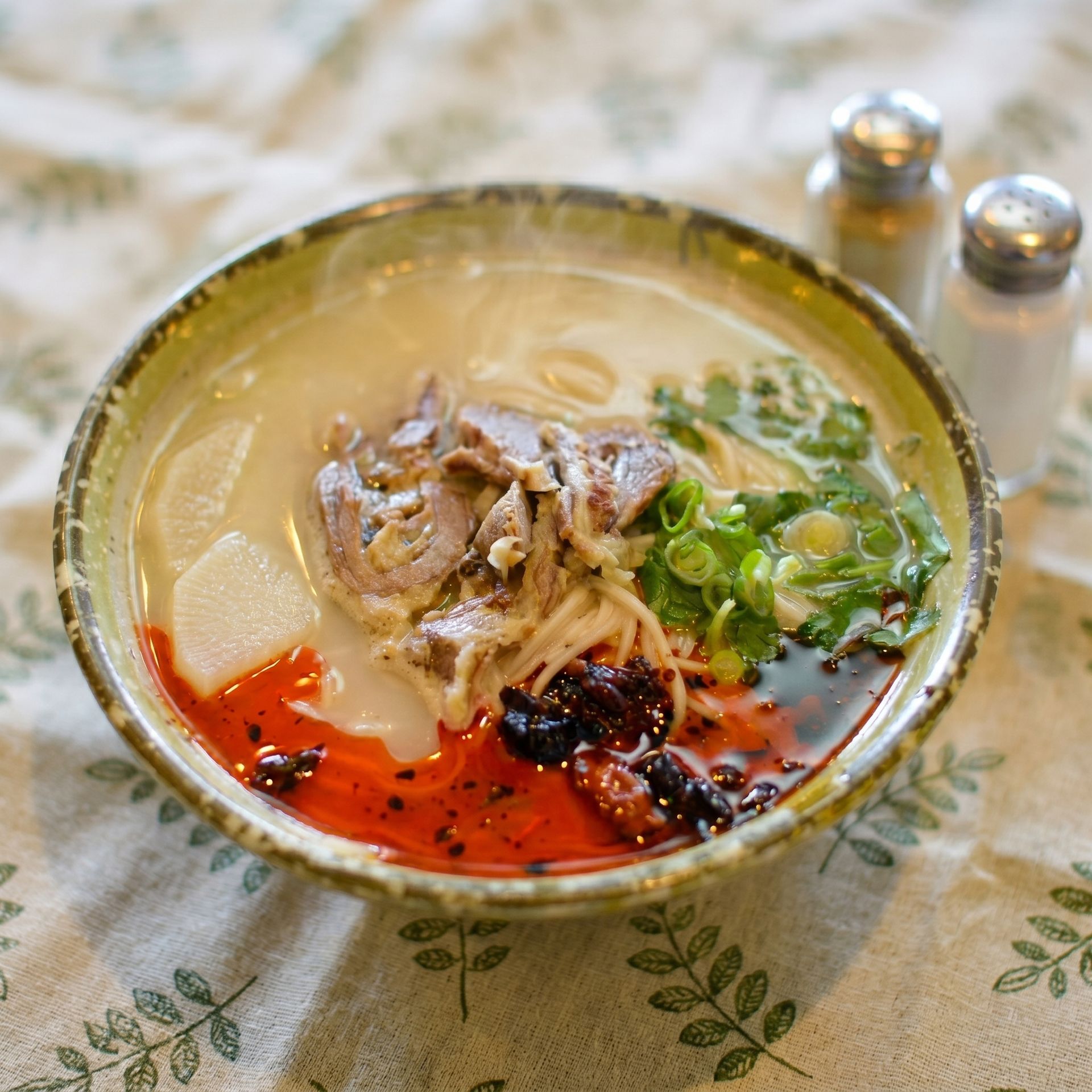 Bowl of spicy soup with meat, greens, and red chili oil on a table
