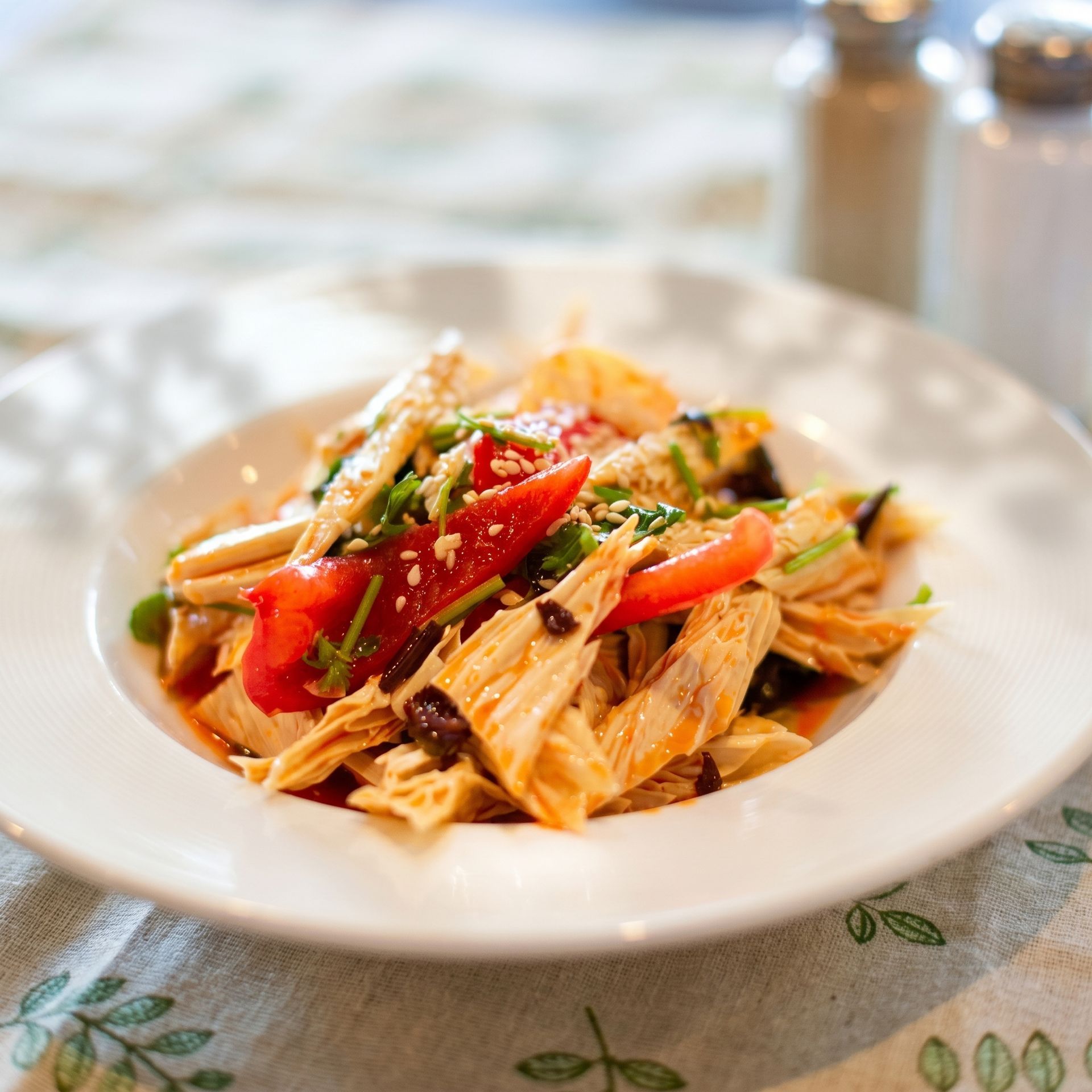 Plate of shredded chicken with red peppers and herbs on a dining table