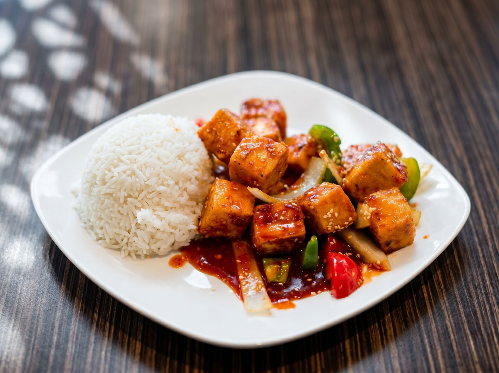 White rice with saucy stir-fried tofu and vegetables on a white plate