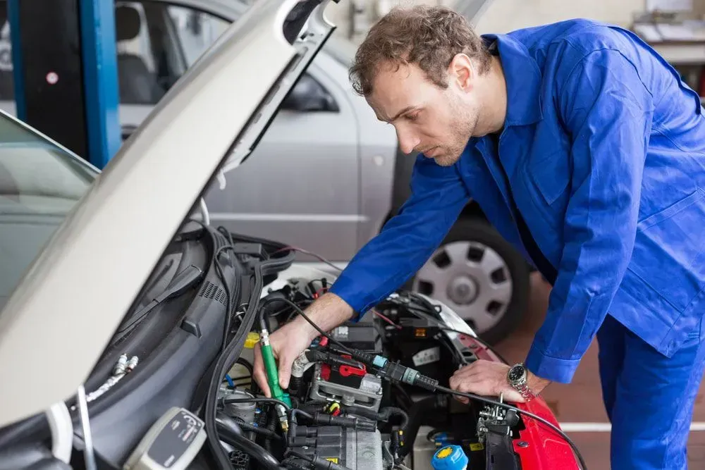 Mechanic in Blue Coveralls Working on a Car Engine in a Garage — Carline Automotive and Exhausts in Belmont, NSW