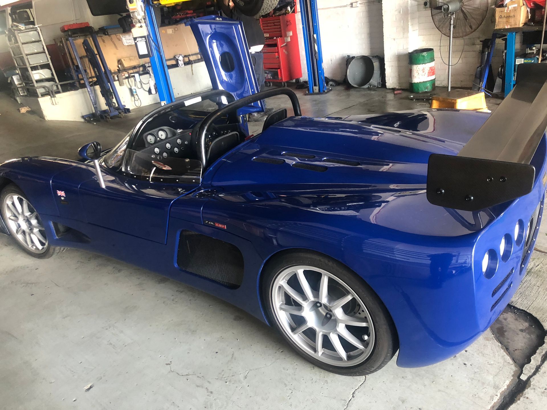 Blue sports car in a garage with the hood and door open.