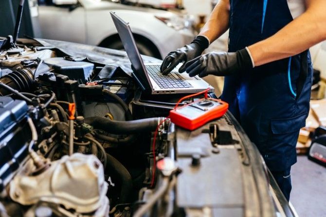 Mechanic using a laptop to diagnose a car engine in a garage, with tools on the engine bay