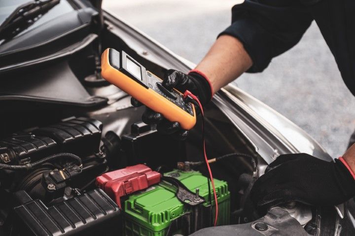 Mechanic using jumper cables to start a car battery under the hood