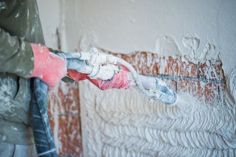 A man is plastering a wall with a machine.
