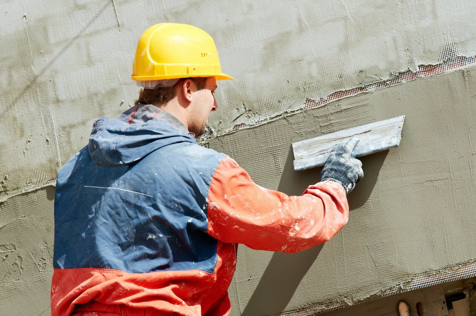 A man wearing a hard hat is plastering a wall with a trowel.