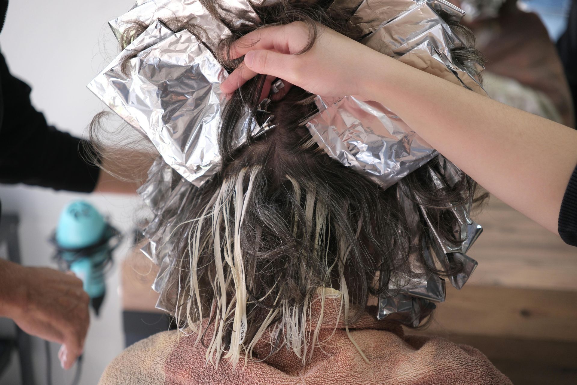 Hairdresser applying foils to a person's hair for highlights. Light blonde dye is visible on the hair.