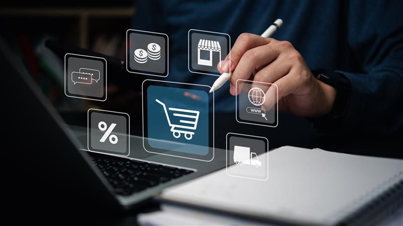Mão usando caneta stylus em um tablet com ícones flutuantes de compras, finanças e análises em um fundo escuro.