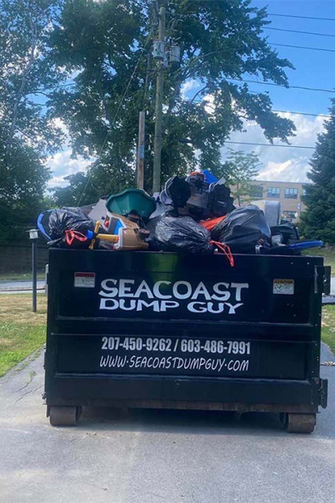 Black dumpster filled with trash bags. 
