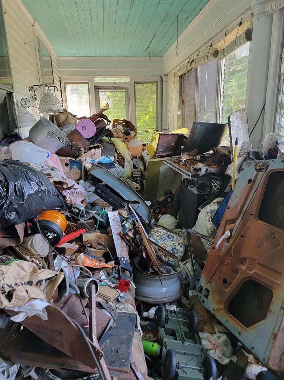 Cluttered porch filled with miscellaneous items: trash, car door, appliances, and toys. Light green ceiling.