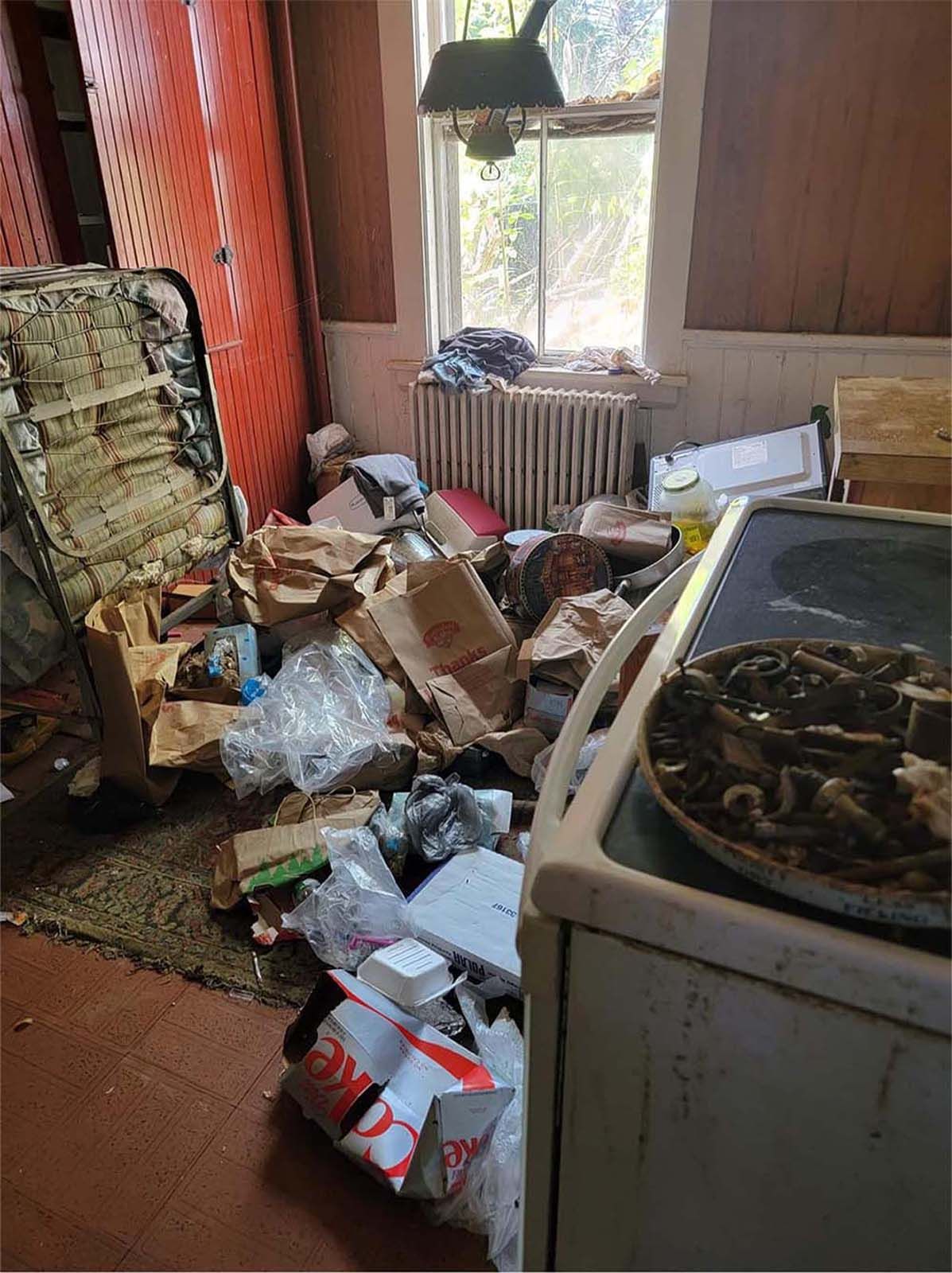 Messy room with trash, boxes, and an old stove. Window visible with light coming in.