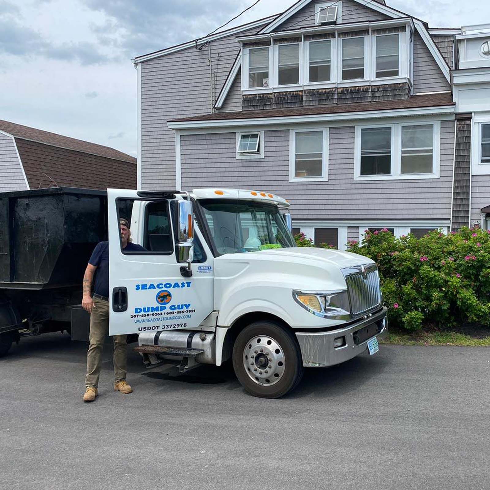 Man standing by a white Sea Coast Dump Guy truck in front of a house.