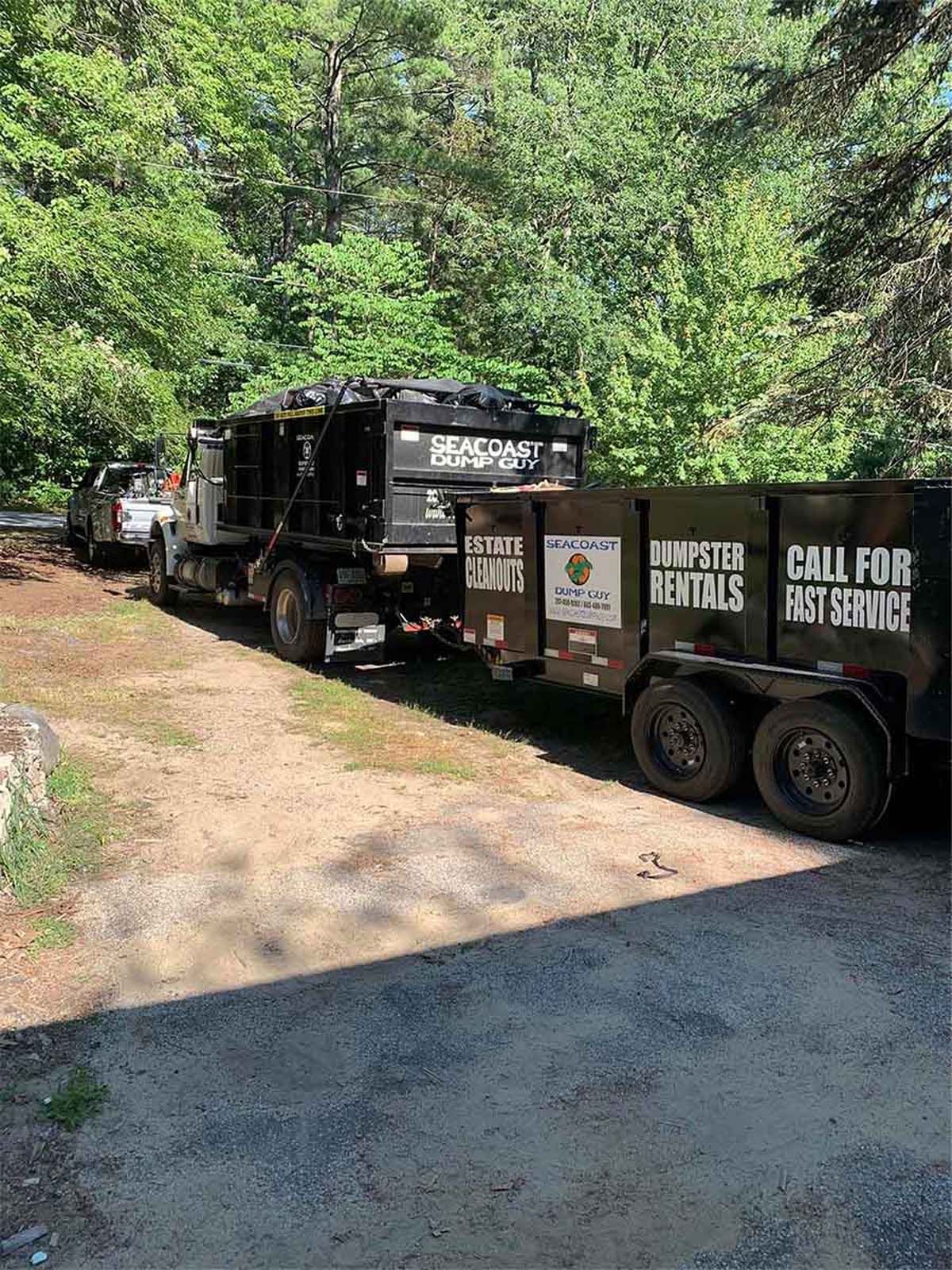 Dump truck with trailer, black, parked on a dirt road, trees in the background, text 