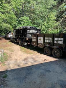 Dump truck with trailer, black, parked on a dirt road, trees in the background, text 