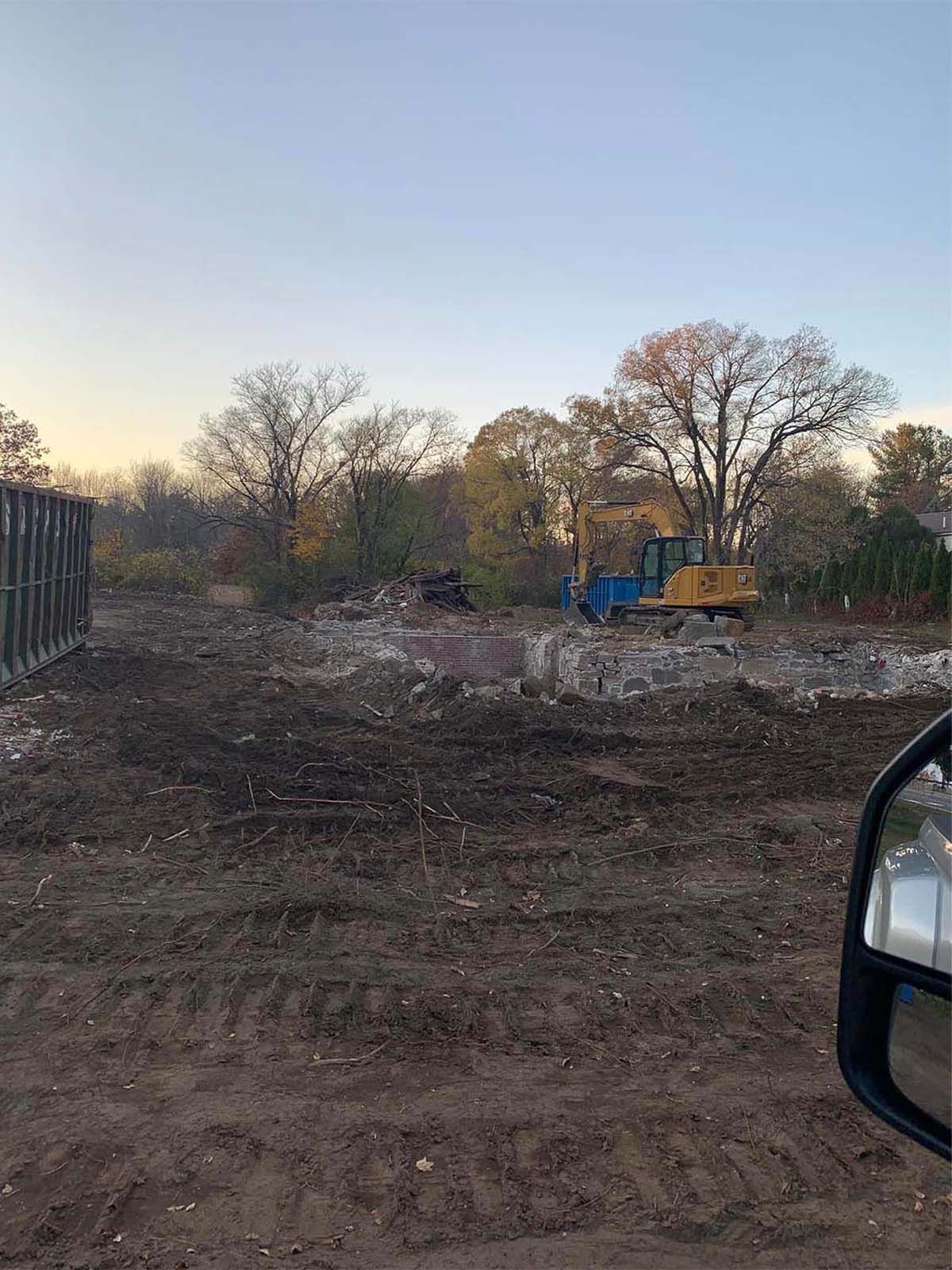 Construction site with excavator. Dirt ground, trees in the background, and a blue and yellow excavator working.