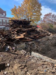 Pile of demolition debris, including wood and concrete, on a construction site. Autumn foliage in background.