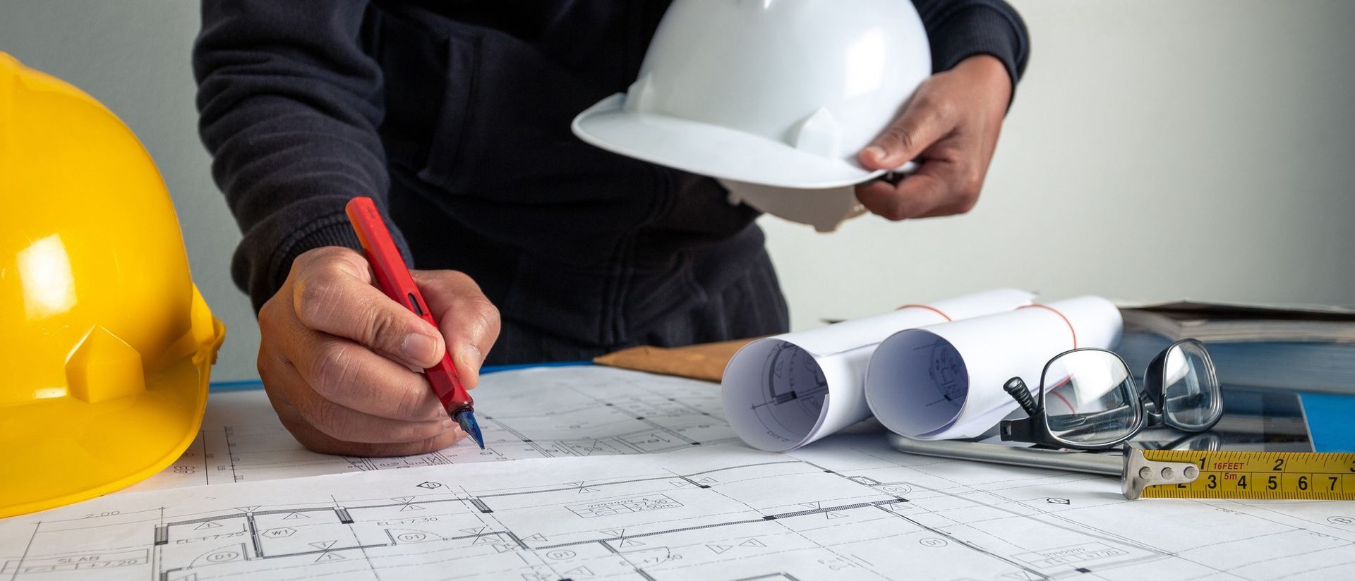 A man is writing on a piece of paper while holding a hard hat.