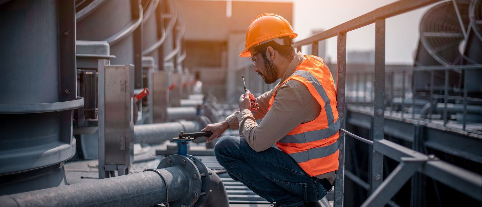 A man in an orange vest and hard hat is working on a pipe.